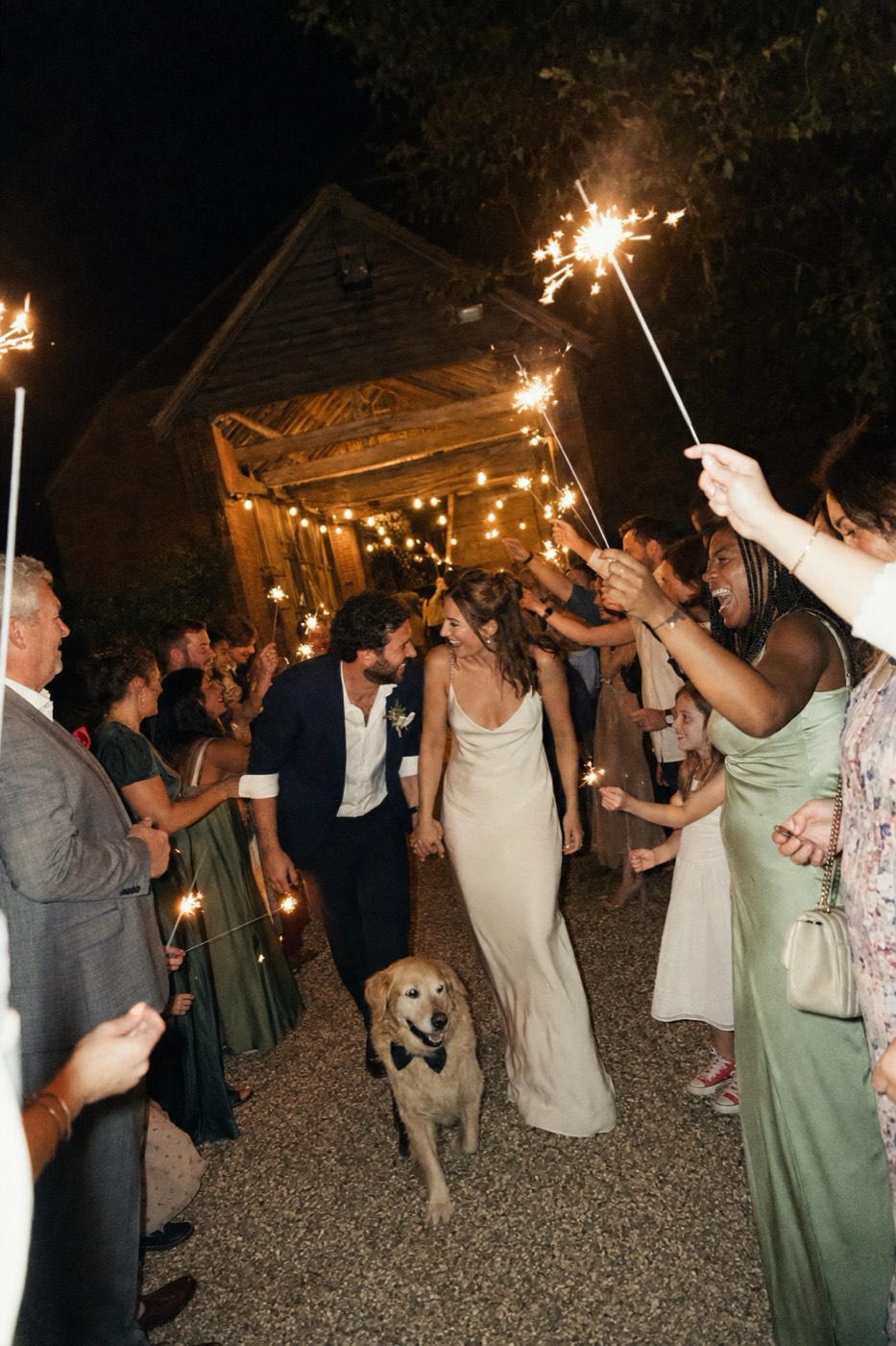 Guests holding lit sparklers up in two lines outside the barn, their faces lit from below by the sparks